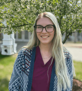 Madison Scampini, RN, BSN – Wachusett Respiratory Care Unit Manager Outdoor portrait of Madison Scampini, RN, BSN, smiling in front of greenery at Holden Rehabilitation & Skilled Nursing Center.